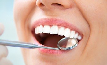 Close up of dental mirror next to a person smiling