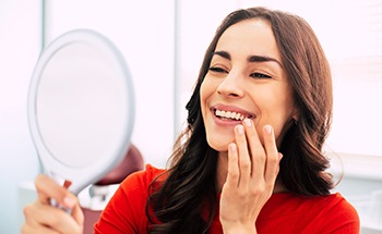 Woman in red-orange shirt smiling at reflection in mirror