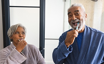 Man and woman with gray hair in bathrobes brushing teeth