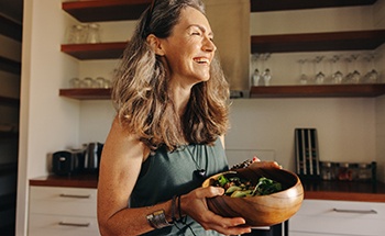 Smiling woman carrying wooden bowl with healthy salad