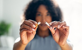 Woman blurry in background breaking cigarette in half in foreground