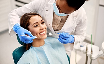 Woman in dental chair smiling as dentist approaches to examine her teeth