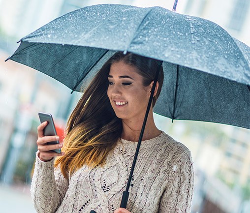 Smiling woman holding umbrella while looking at phone