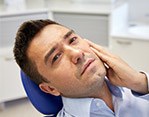 Man in dental chair holding side of jaw in pain