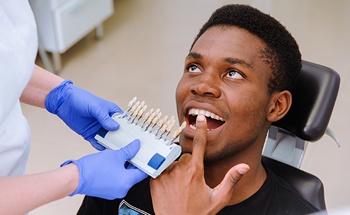 Man in dental chair smiling next to tooth color chart