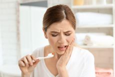 Woman touching her cheek in pain who needs to see an emergency dentist